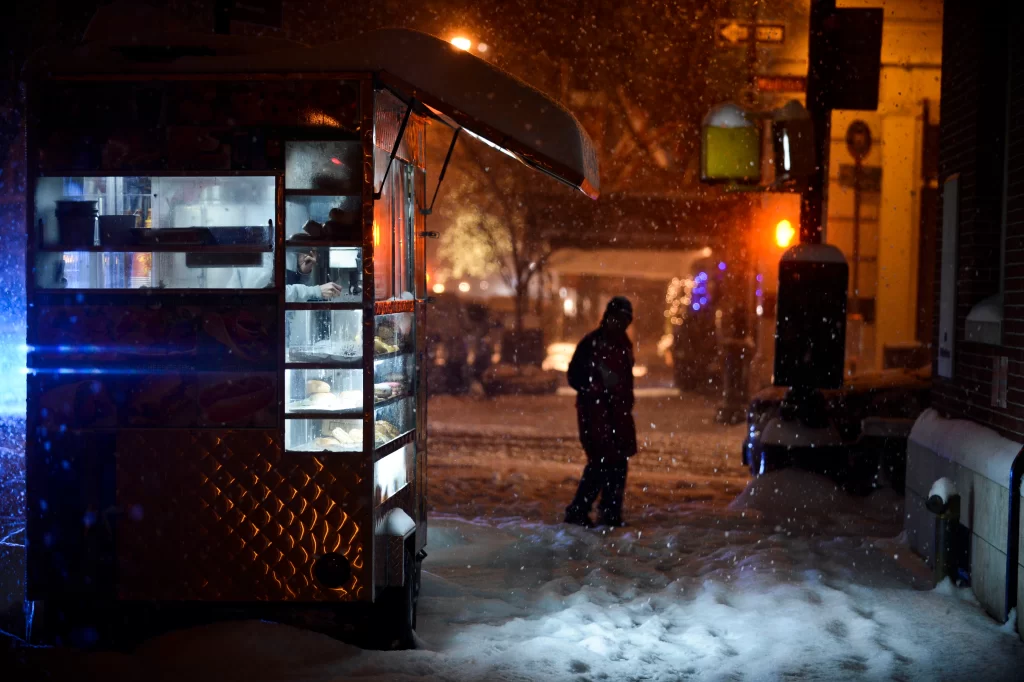 Halal cart in the snow storm with a figure silhouetted against the lights of the street..